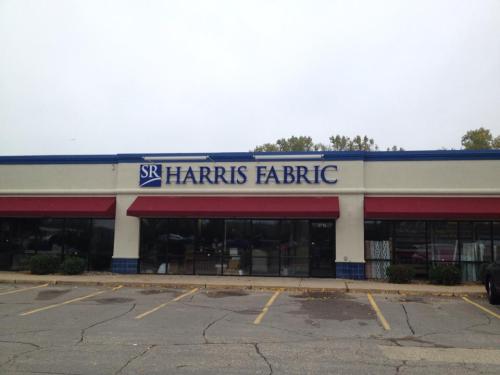 Storefront of Harris Fabric with a blue and white sign, red awnings, and a cloudy sky above.