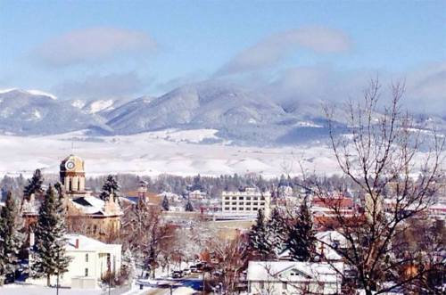 Snow-covered landscape with mountains in the background, featuring a clock tower and trees in the foreground.