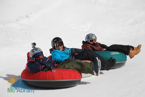 Three people in winter gear sit on colorful snow tubes, ready to slide down a snowy slope.