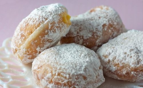 A plate of powdered sugar-dusted donuts, some filled with cream, on a delicate lace doily.