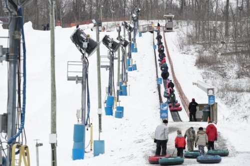 A snowy hill with people riding inflatable tubes down a slope, surrounded by snow and ski lift equipment.
