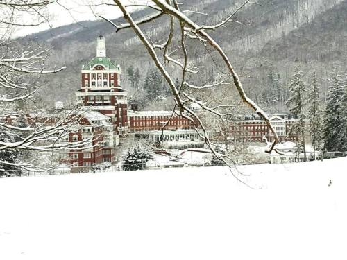 A snow-covered landscape featuring a large historic building surrounded by trees and mountains in winter.