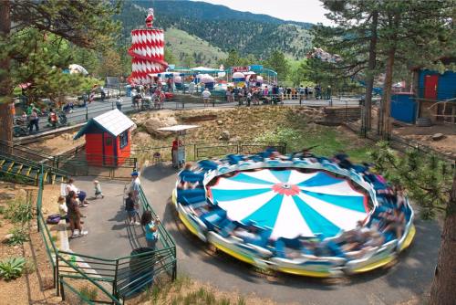 A colorful amusement park scene with a spinning ride, surrounded by trees and mountains in the background.