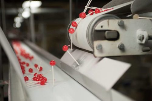 Lollipops on a conveyor belt, with red candy and sticks visible, moving through a production facility.