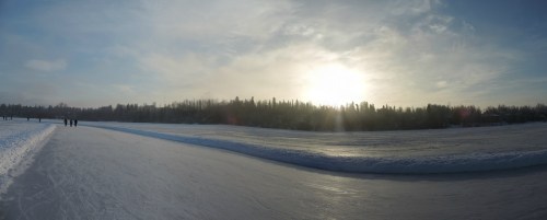 A panoramic view of an icy landscape with a frozen path, trees in the background, and a bright sun setting in the sky.