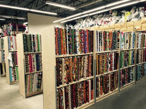 A fabric store interior with shelves filled with colorful rolls of fabric and stacks of materials overhead.