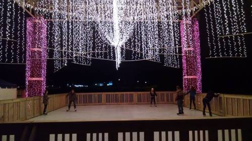 A skating rink illuminated by colorful lights, with people skating under a festive canopy at night.