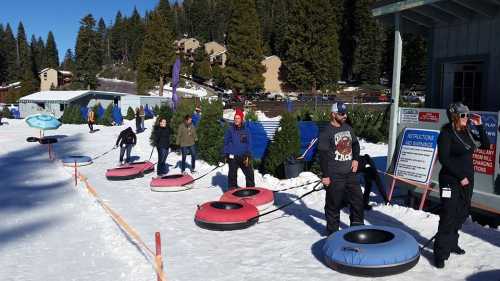 People tubing on snow, pulling inflatable tubes, with a snowy landscape and trees in the background.