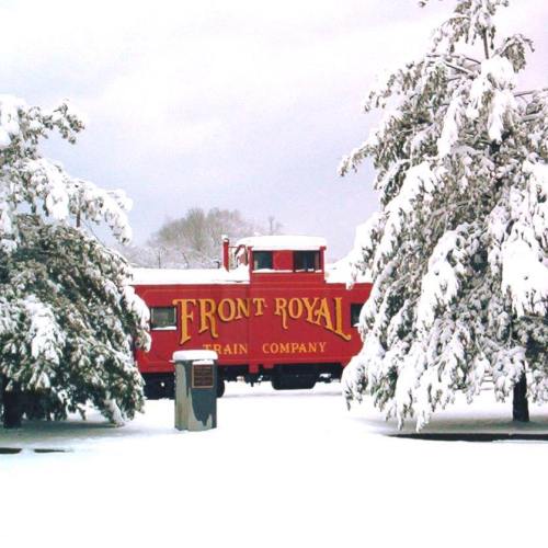 A red train car labeled "Front Royal Train Company" surrounded by snow-covered trees in a winter landscape.