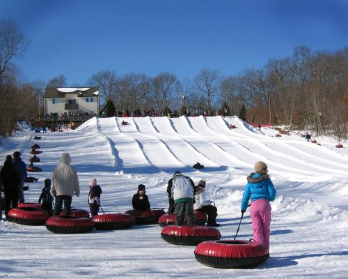 A snowy hill with people tubing, some climbing up while others slide down, under a clear blue sky.