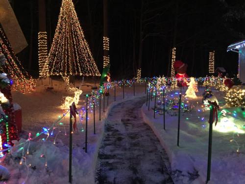 A snowy path lined with colorful Christmas lights and decorations, leading through a festive winter scene.