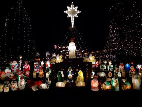A festive display of illuminated Christmas decorations, featuring snowmen, angels, and a large star atop a tree.