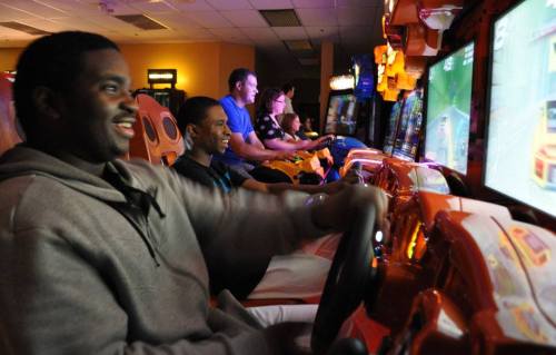 A group of people enjoying racing arcade games, focused and smiling while playing.
