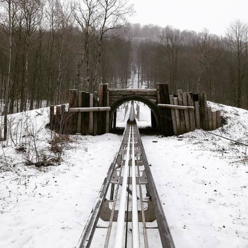 A snowy landscape featuring a wooden bridge over a set of metal tracks leading into the distance.