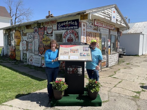 Two people stand beside an informational display in front of a vintage building covered in colorful signs.