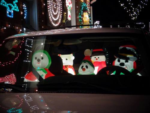 A festive scene inside a car with inflatable snowmen and holiday decorations glowing in the night.
