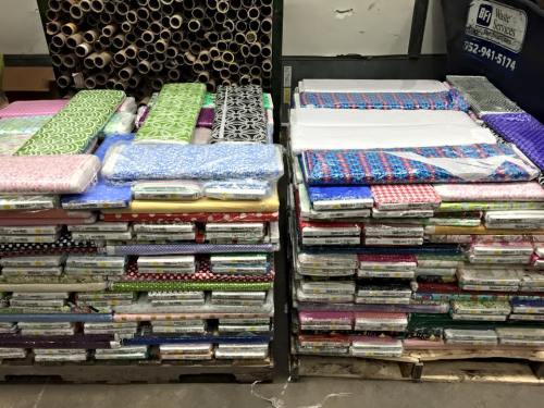 Stacks of colorful fabric rolls neatly arranged on pallets in a storage area.