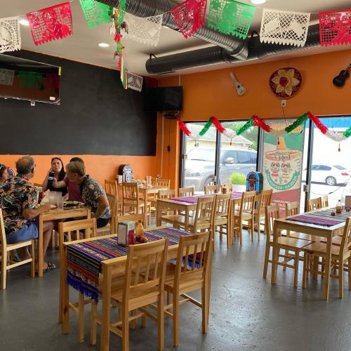 A colorful restaurant interior with wooden tables, festive decorations, and patrons enjoying their meals.