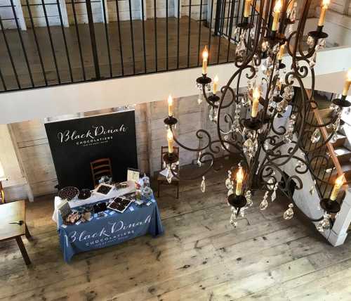 A spacious room with a chandelier, featuring a table displaying chocolates and a sign for "Black Dinah Chocolatiers."