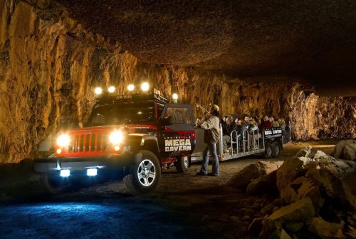 A tour vehicle inside a cavern, with passengers boarding under a rocky ceiling illuminated by lights.