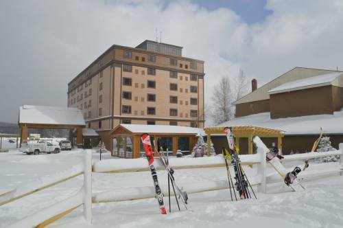 A snowy scene featuring a hotel and ski equipment in front, with a cloudy sky overhead.