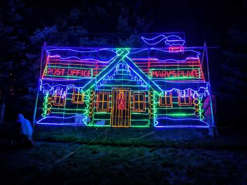 A brightly lit, festive display of a post office and "Marv's Place" with colorful neon lights against a dark background.