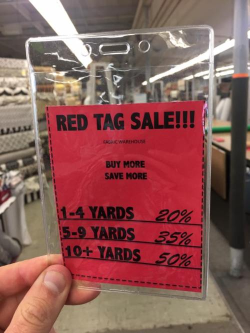A hand holds a red sale sign offering discounts on fabric: 20% off 1-4 yards, 35% off 5-9 yards, 50% off 10+ yards.
