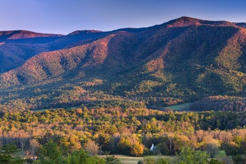 Vibrant autumn landscape with rolling mountains and colorful trees under a clear sky.