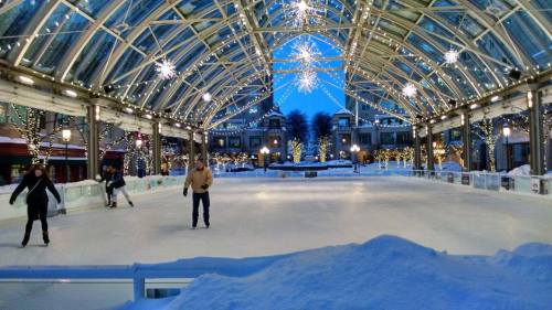 A festive indoor ice skating rink with twinkling lights and snow, surrounded by holiday decorations.