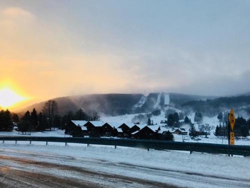 Snow-covered landscape at sunset, featuring a ski slope and cozy cabins in the foreground.