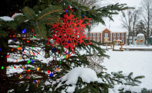 A snowy scene featuring a decorated Christmas tree with colorful lights and snowflake ornaments in the foreground.