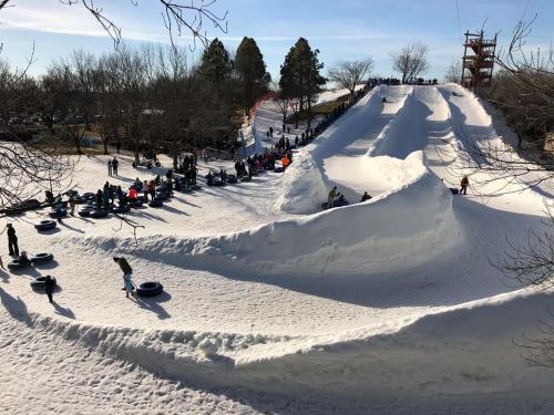 A snowy hill with multiple tubing lanes and people enjoying winter activities under a clear blue sky.