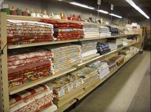 A store aisle filled with neatly stacked rolls of various patterned fabrics on shelves.
