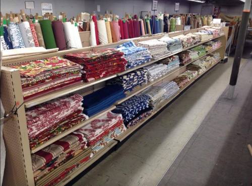 A fabric store aisle with shelves stacked with colorful rolls of fabric in various patterns and textures.