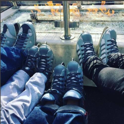 A group of feet in ice skates resting near a fire pit, with flames and glass stones in the background.