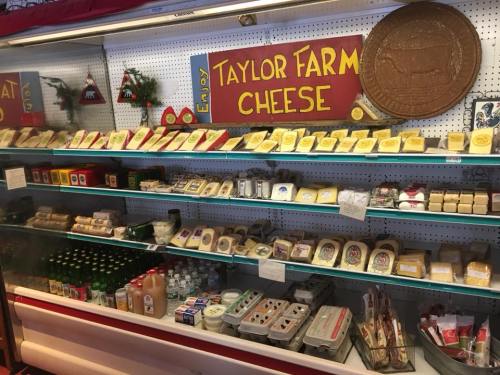 A display case filled with various cheeses and dairy products, labeled "Taylor Farm Cheese," decorated for the holidays.