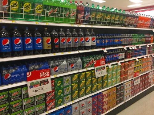 A grocery store shelf filled with various soda brands, including Pepsi, Mountain Dew, and other soft drinks.
