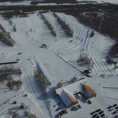 Aerial view of a snowy ski resort with slopes, ski lifts, and a lodge surrounded by trees.