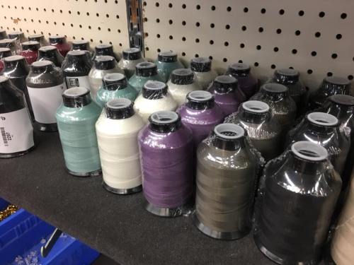 A row of colorful spools of thread neatly arranged on a shelf, with various shades of blue, green, white, and purple.