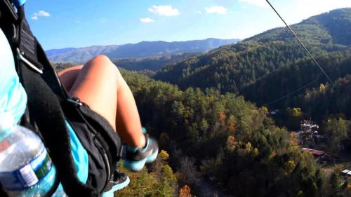 A person's leg hangs over a zip line, with a scenic view of mountains and trees in the background.