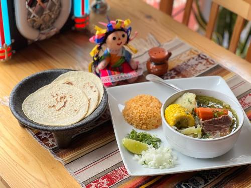 A colorful Mexican meal featuring soup, rice, tortillas, lime, and a decorative doll on a vibrant table setting.