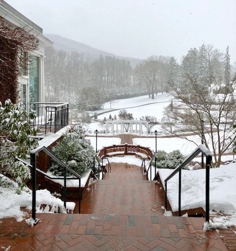 A snowy scene showing brick steps leading down to a winter landscape with trees and a distant pavilion.