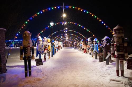 A snowy pathway lined with colorful lights and large nutcracker figures, creating a festive holiday atmosphere.