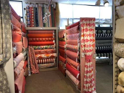 A fabric store aisle filled with colorful rolls of patterned textiles and curtains stacked on shelves.