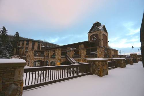 A snow-covered building with stone architecture and a clock tower, surrounded by trees under a cloudy sky.