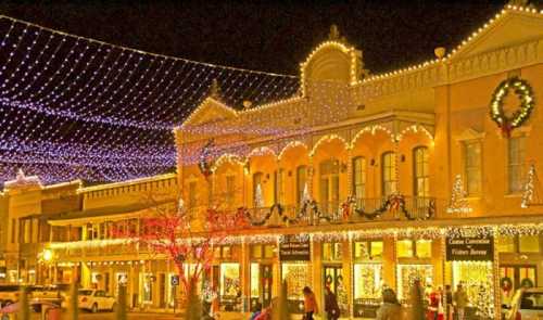 A festive street scene at night, adorned with colorful holiday lights and decorations on buildings.