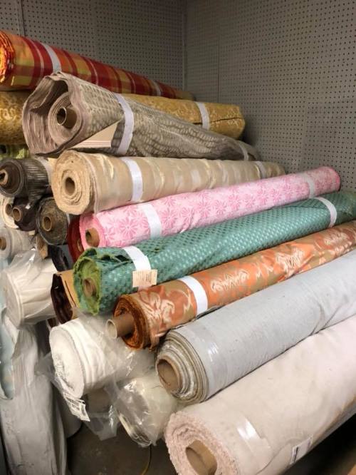 A stack of various fabric rolls in different colors and patterns, neatly arranged in a storage area.