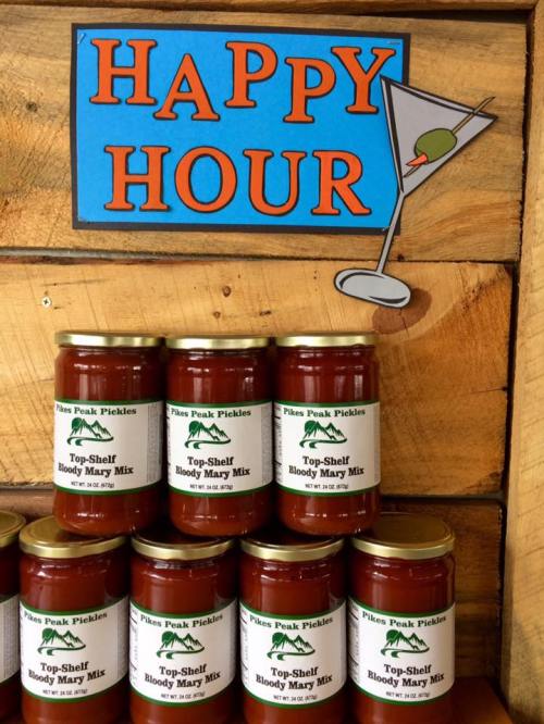 Jars of Bloody Mary mix displayed on a wooden shelf with a "Happy Hour" sign and a martini graphic above.