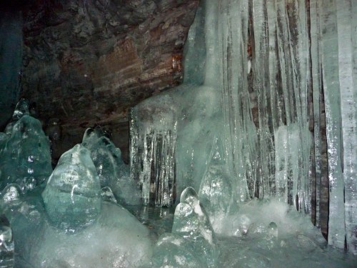 Ice formations in a cave, featuring sharp icicles and smooth, frozen surfaces reflecting light.