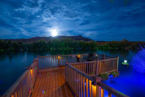 A serene lakeside deck under a full moon, surrounded by mountains and illuminated by soft blue lights.